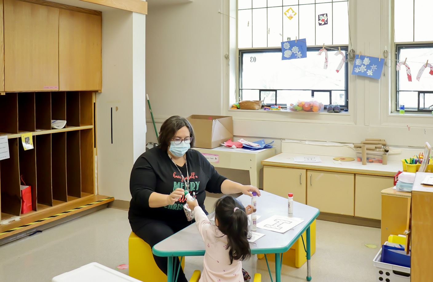 A teacher and a student work on a craft at a table