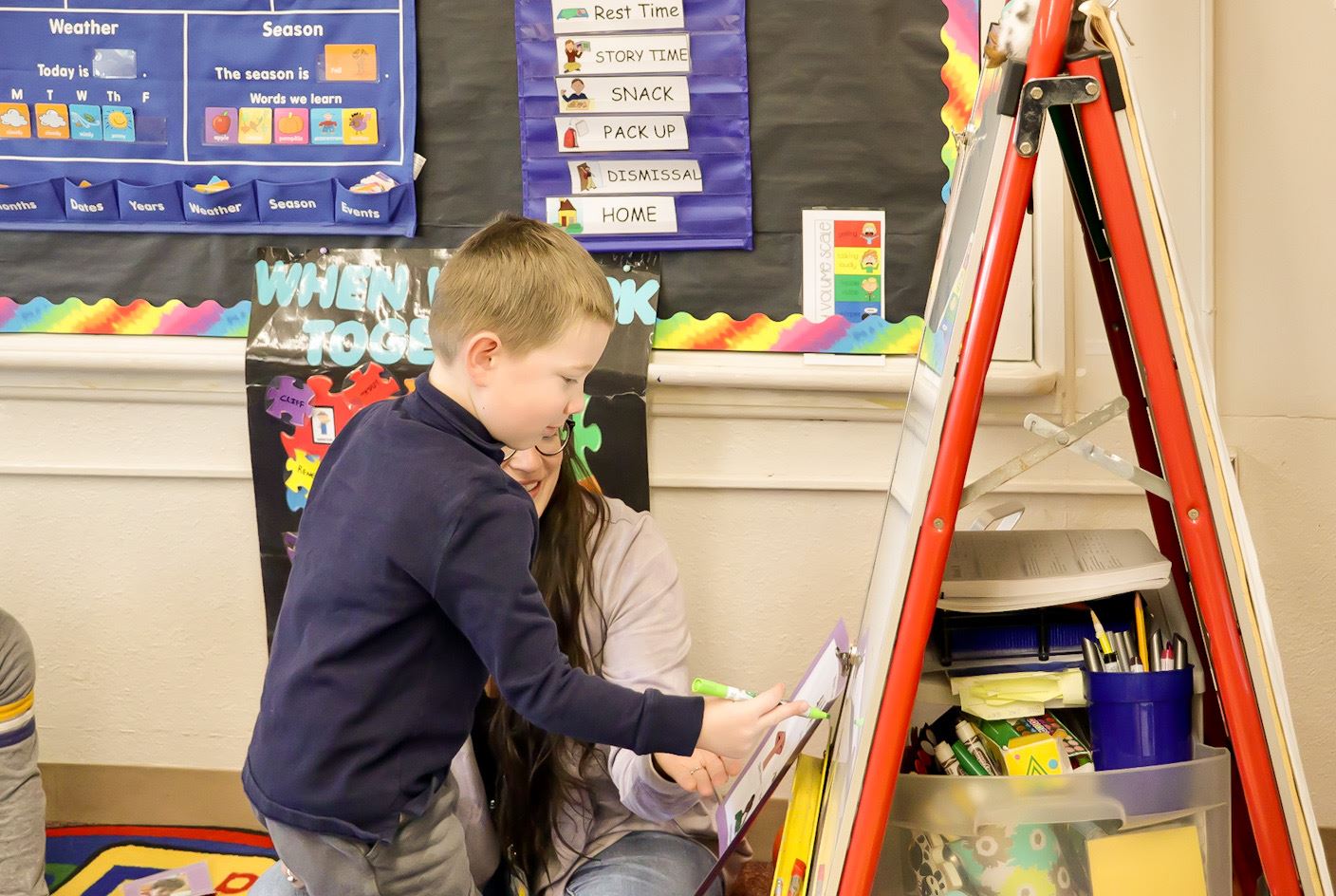 A teacher watches on as a student a writes on a poster board