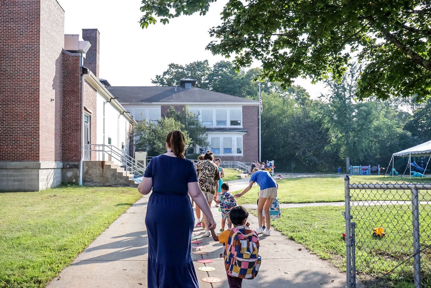 A teacher holds a student's hands as they walk down the sidewalk of Ashand Preschool